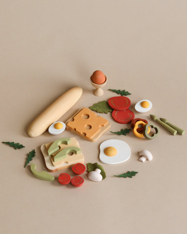 An assortment of Sabo Concept Handmade Wooden Breakfast Set - Vegetarian items, including bread, cheese, eggs, and vegetables, artistically crafted from non-toxic materials, arranged neatly on a beige background.