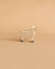 A wooden toy sheep with a light tan body, grey hooves, and subtle circular patterns is standing on a beige background. Handcrafted in Europe, this Holztiger Lamb boasts a simple and minimalist design.