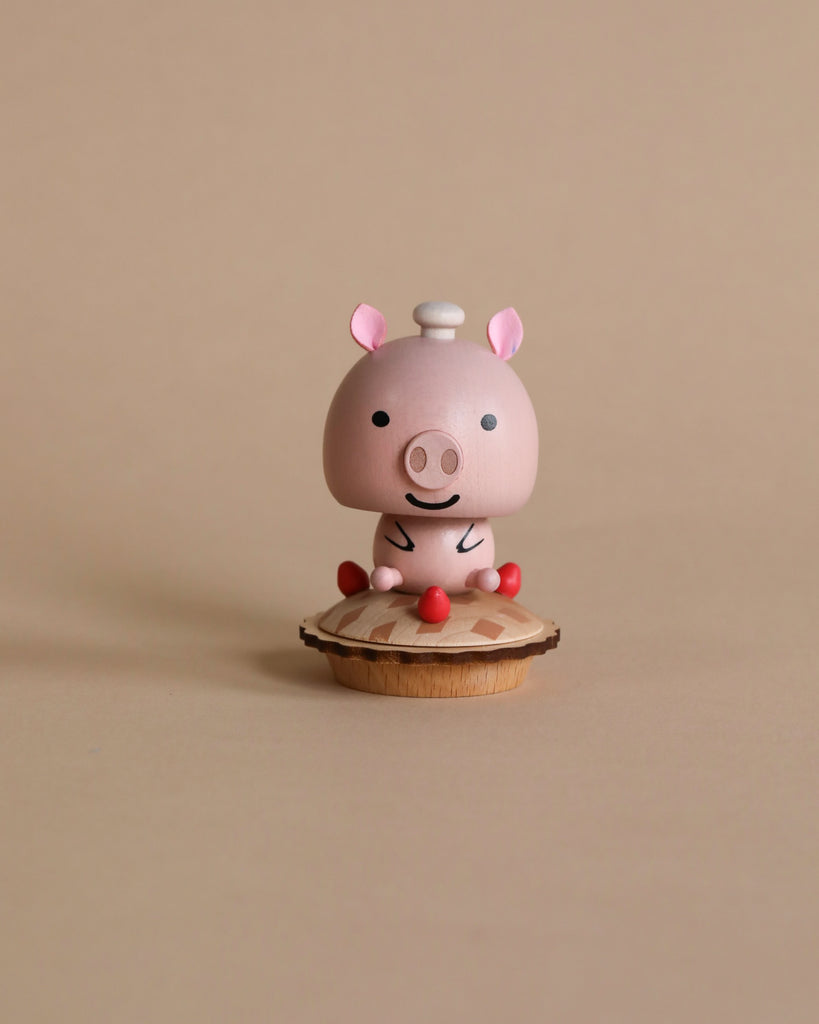 A Wooden Pig Bobblehead stands on a wooden base, radiating joy with squinted eyes and a wide, cheerful smile, enhanced by simple rosy cheeks. A white chef's hat