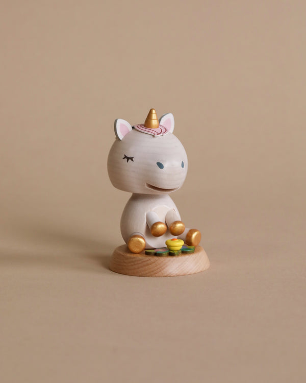 A small Wooden Unicorn Bobblehead figurine of a smiling unicorn cat, painted white with gold hooves and a pink-gold spiral horn, sitting on a wooden base surrounded by tiny fake gold coins.