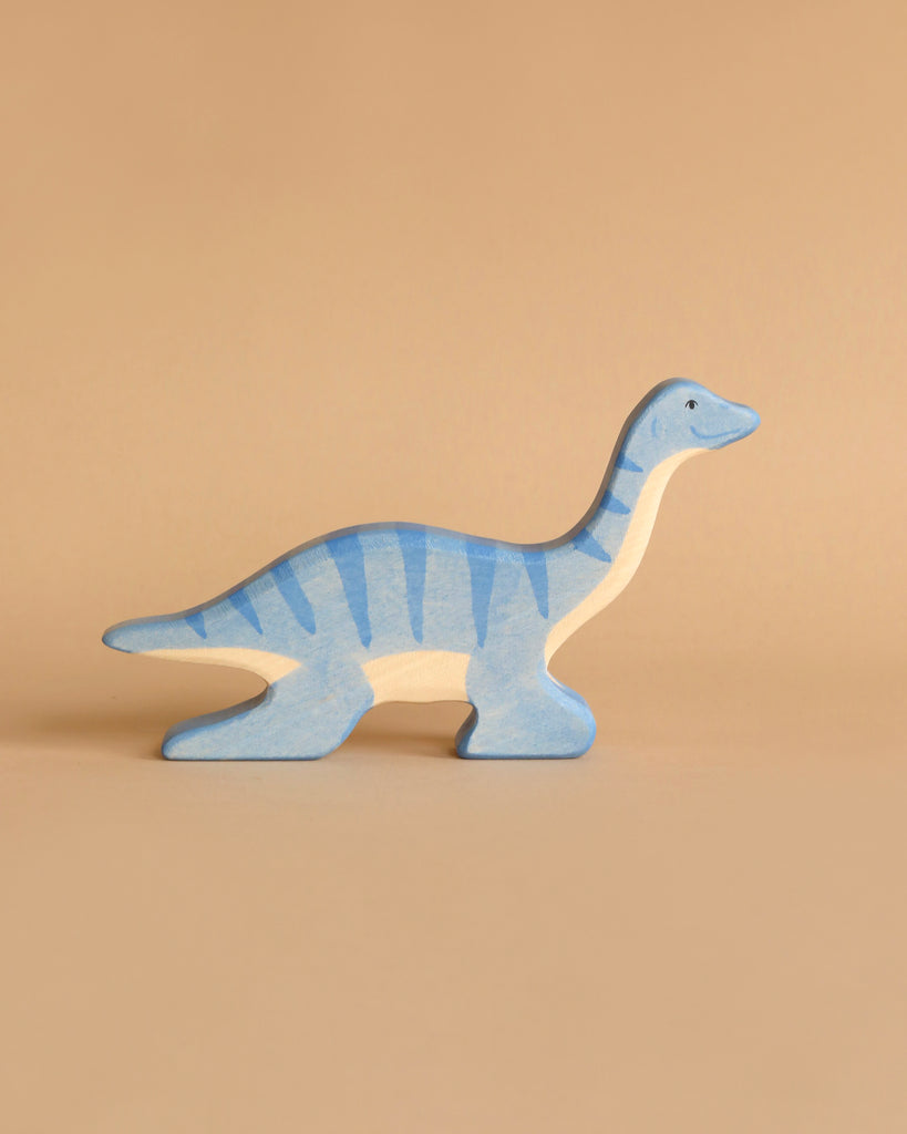 A Holztiger Plesiosaurus Dinosaur, crafted from maple and beech wood and painted in shades of blue and light beige, stands against a plain beige background. The dinosaur has a long neck and tail, exemplifying the simple, handcrafted design characteristic of HOLZTIGER figures.