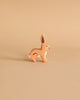 A handcrafted wooden rabbit from the Holztiger Handmade Wooden Woodland Animals Set, painted in natural brown with white accents, sits on a beige background—perfect for open-ended play and classic in style.