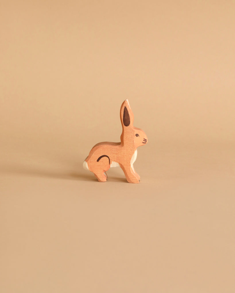 A handcrafted wooden rabbit from the Holztiger Handmade Wooden Woodland Animals Set, painted in natural brown with white accents, sits on a beige background—perfect for open-ended play and classic in style.