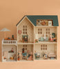 The Maileg Fully Furnished Dollhouse Set + Gift With Purchase features multiple rooms filled with miniature furniture, accessories, and animal dolls posed in daily life scenes, all set against a soft beige background.