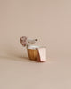 The Maileg Little House Bathroom Set features a small stuffed dog with a textured hat in a gold bowl, next to miniature mouse furniture and a pink-striped towel, all set against a beige background.