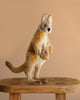 The Kangaroo Mom Stuffed Animal, featuring a baby joey in its pouch and crafted in the style of HANSA animals, stands on a wooden stool against a plain beige background.