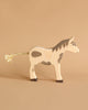 A handcrafted wooden Holztiger Horse, Mustang toy with painted gray spots stands against a plain beige background. This HOLZTIGER figure boasts a braided rope tail and detailed facial features, reflecting the exquisite craftsmanship for which these Made in Europe toys are renowned.