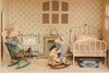 Two toy mice enjoy the Maileg Fully Furnished Dollhouse Set + Gift With Purchase. One mouse sits in a rocking chair, another rides a wooden rocking horse, surrounded by a bed, crib, clock, and suitcase against patterned wallpaper.