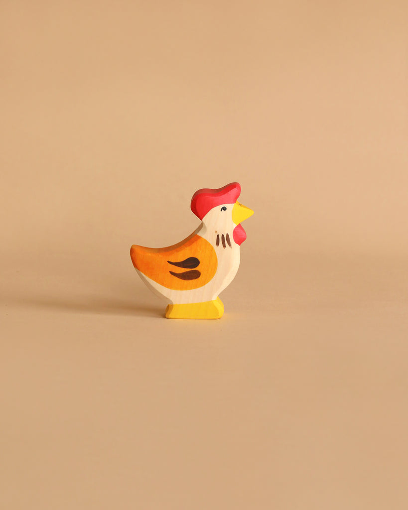 A Holztiger Handmade Wooden Farm Animals Set toy hen, painted yellow, orange, and white with a red comb, is displayed on a plain beige background.
