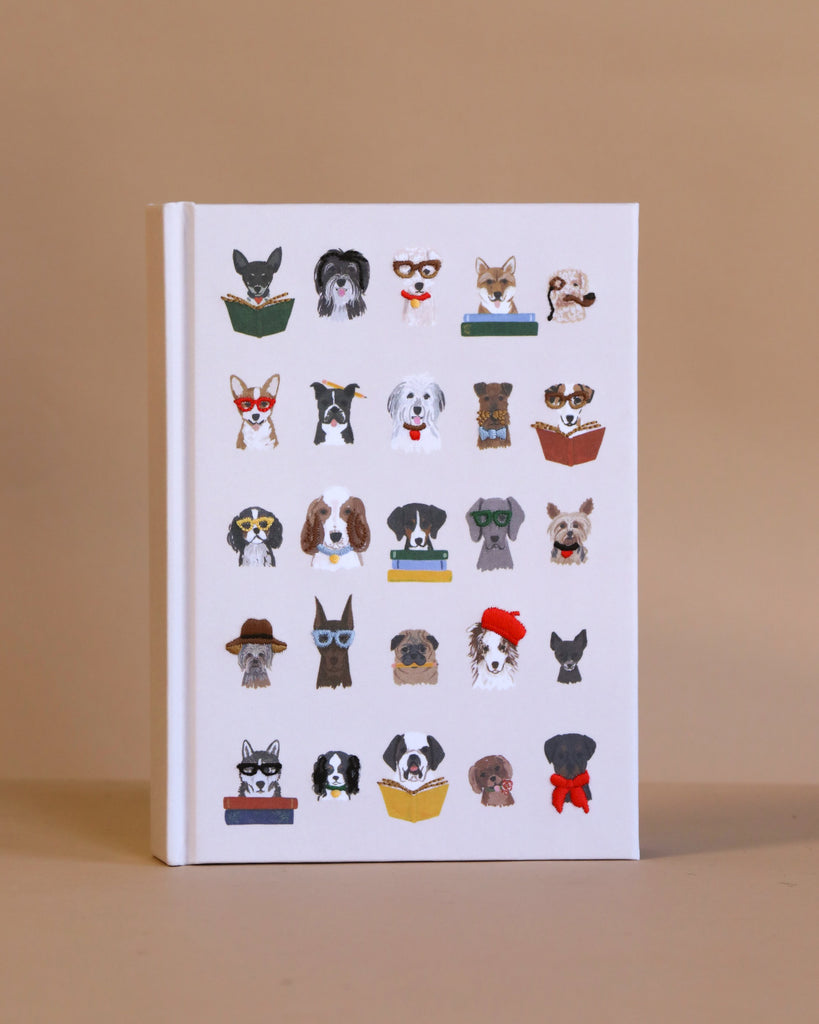 The Studious Dogs Embroidered Journal is a white personal diary with an embroidered cover of illustrated dogs wearing glasses, hats, and reading books, arranged in four rows on a plain beige background.