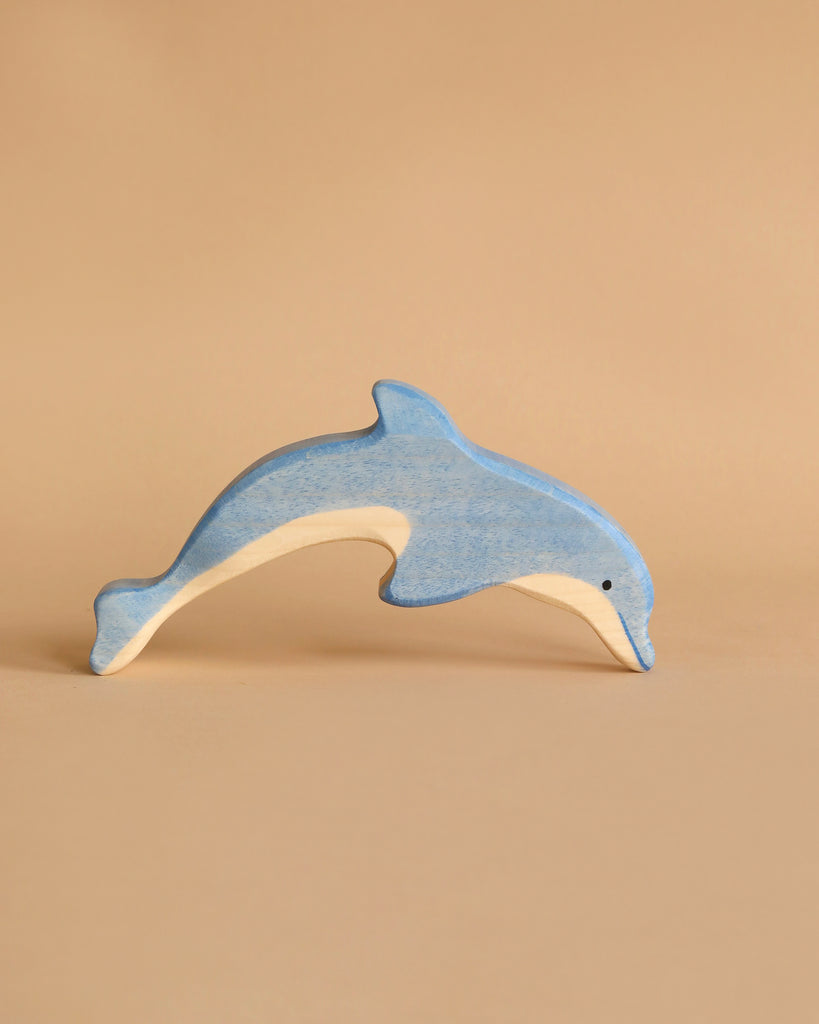 A small blue dolphin from the Holztiger Handmade Wooden Ocean Animals Set has a natural wood underside and is shown against a plain beige background.