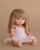 The Minikane Baby Doll (13") - Nina with Clothing features long, straight light brown hair and bangs. Made in Spain, this anatomically correct doll wears a pale pink dress with a tulle skirt and sits barefoot against a beige background.