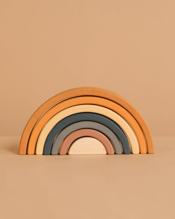 The Handmade Rainbow Stacker - Mustard features five wooden arches in muted earth tones, crafted with non-toxic paint for safe play. Arches stack from largest to smallest and are pictured on a beige background.