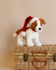 A Steiff Snuffy Puppy Dog plush, featuring a festive Santa hat, stands proudly on a woven wicker basket. The soft beige background enhances the warm tones of this charming scene.