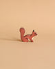 A small, handcrafted wood toy figurine of a squirrel with a bushy tail is placed on a light brown background. Made in Europe, the squirrel is painted in earthy tones of reddish-brown with minimal detailing for facial features and the texture of its fur. This charming piece is reminiscent of the Holztiger Squirrel, Standing.