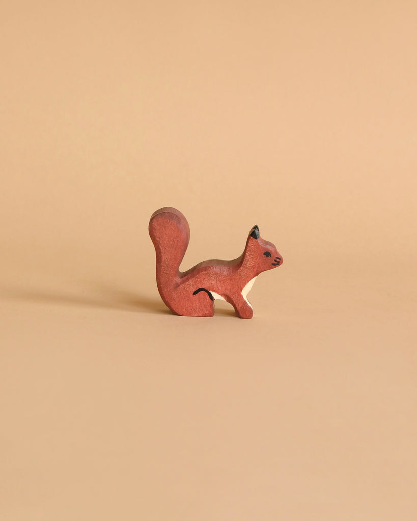 A small, reddish-brown squirrel figurine from the Holztiger Handmade Wooden Animal Play Set stands on a smooth beige surface against a matching background, highlighting the charm of handcrafted wooden toys.