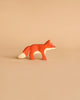 A small, handcrafted fox from the Holztiger Handmade Wooden Woodland Animals Set, featuring orange, white, and red colors, stands on a beige background—ideal for open-ended play and fans of wooden animal figures.