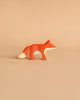 A small, wooden **Holztiger Fox, Small**, handcrafted from maple and beech wood, stands on a plain beige background. The fox is painted in shades of orange with white on the tip of its tail, underbelly, and snout, emphasizing its simple and charming design characteristic of HOLZTIGER figures.