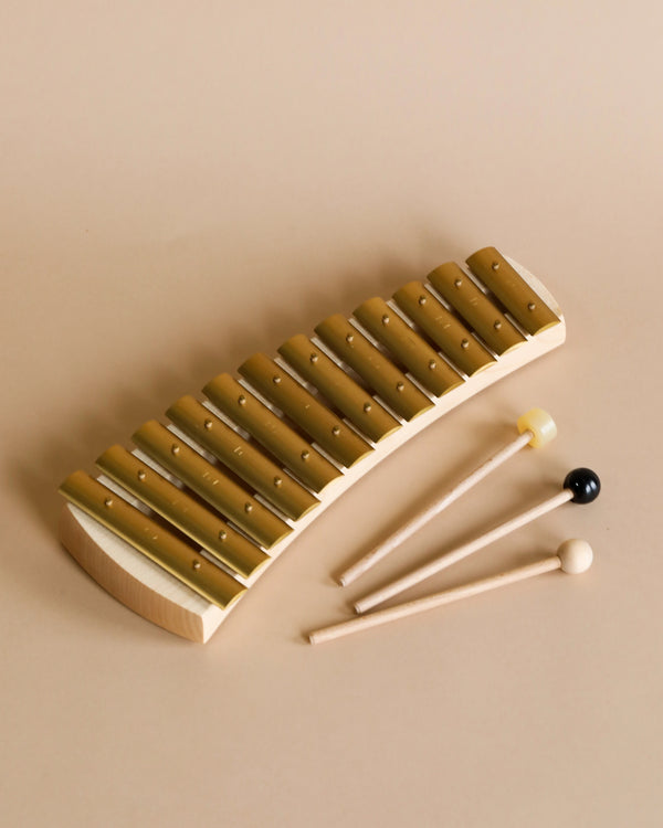 A Auris Xylophone Diatonic with bars arranged in a curve, accompanied by three mallets with different colored tips, placed on a beige background.