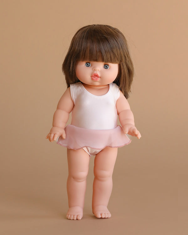 The Minikane Standing Doll (14") - Chléa With Clothing features light skin, straight brown hair, blue eyes, and stands upright in a pale pink leotard with a short skirt against a plain beige background.