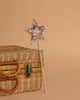 The Easter Basket Gift Set features a glittery star-shaped magic wand with a pink stick, resting against a closed wicker suitcase on a beige background.