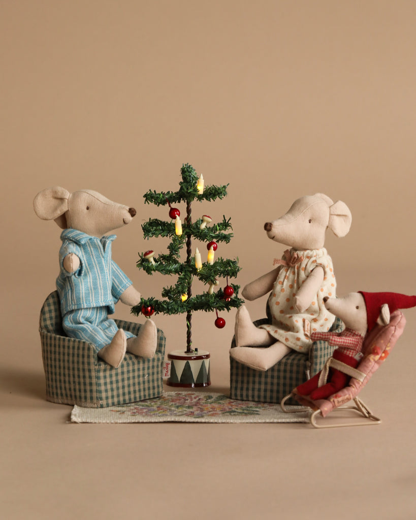 The Maileg Family Christmas Set features three mice with festive furniture around a holiday tree, all arranged on a patterned rug—perfect for cozy storytelling and cheerful holiday scenes.