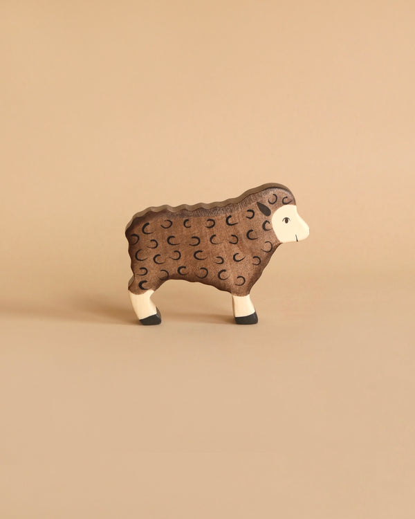 A small, brown Holztiger Brown Sheep, Standing figurine with a woolly texture is shown against a plain beige background. The handcrafted wood sheep has detailed carvings to represent its wool and black hoofs. Made in Europe.