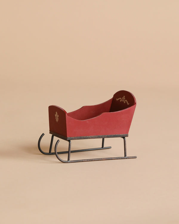 The Maileg Sleigh, Mouse - Red is a small, vintage-style wooden sleigh with metal runners, hand-painted details, and a simple decorative motif on the backrest, shown on a neutral beige background.