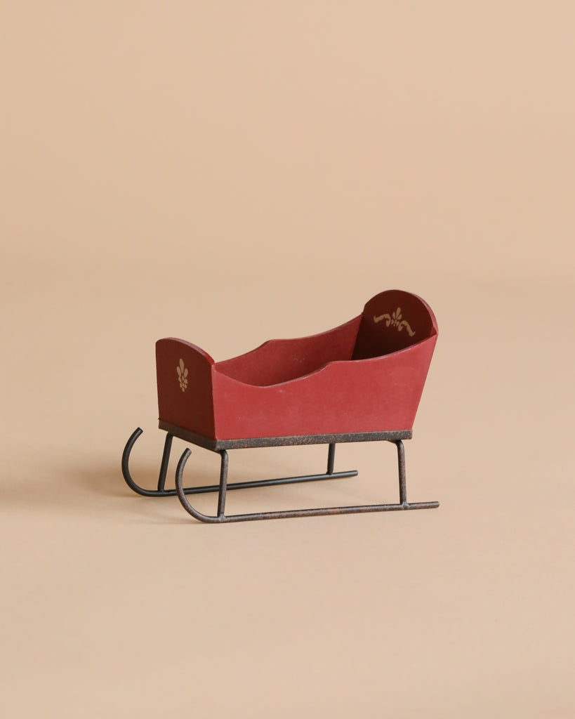 The Maileg Sleigh, Mouse - Red is a small, vintage-style wooden sleigh with metal runners, hand-painted details, and a simple decorative motif on the backrest, shown on a neutral beige background.