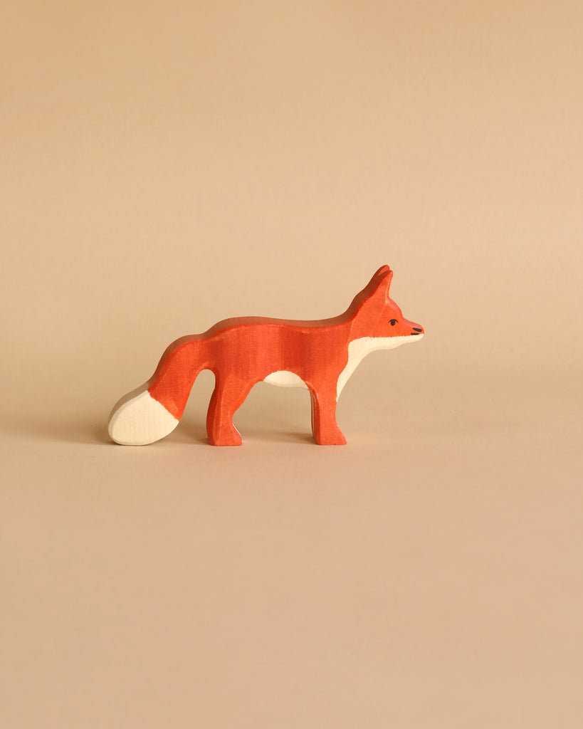 A small, handcrafted wooden **Holztiger Fox, Standing** with a reddish-brown body, white-tipped tail, and pointed ears stands on a plain beige background. This high-quality piece has a minimalist design, highlighting the fox's sleek, elegant silhouette reminiscent of HOLZTIGER figures.