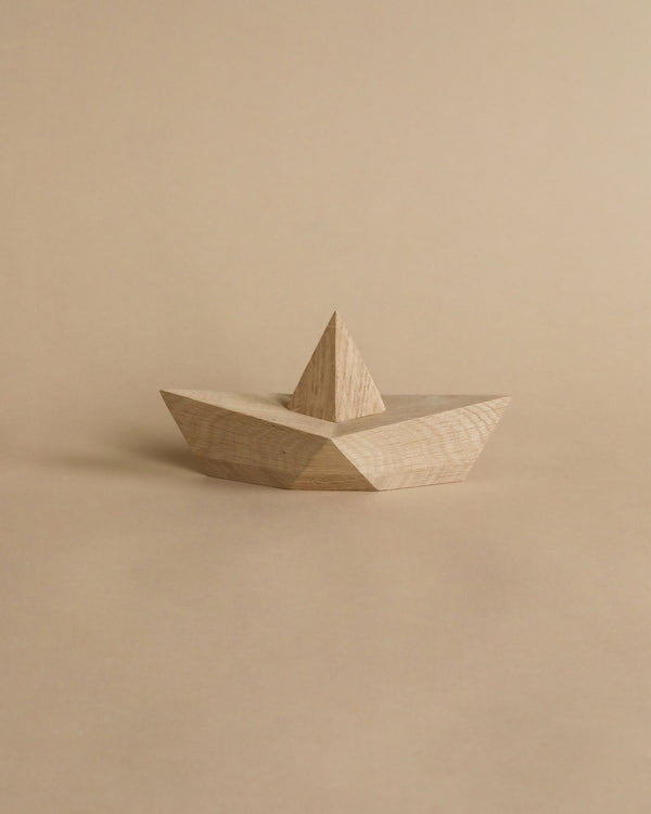 A simple Boyhood Admiral, Large Oak toy boat with a pointed sail, on a plain beige background. The boat has a smooth finish and exhibits natural wood grain textures.