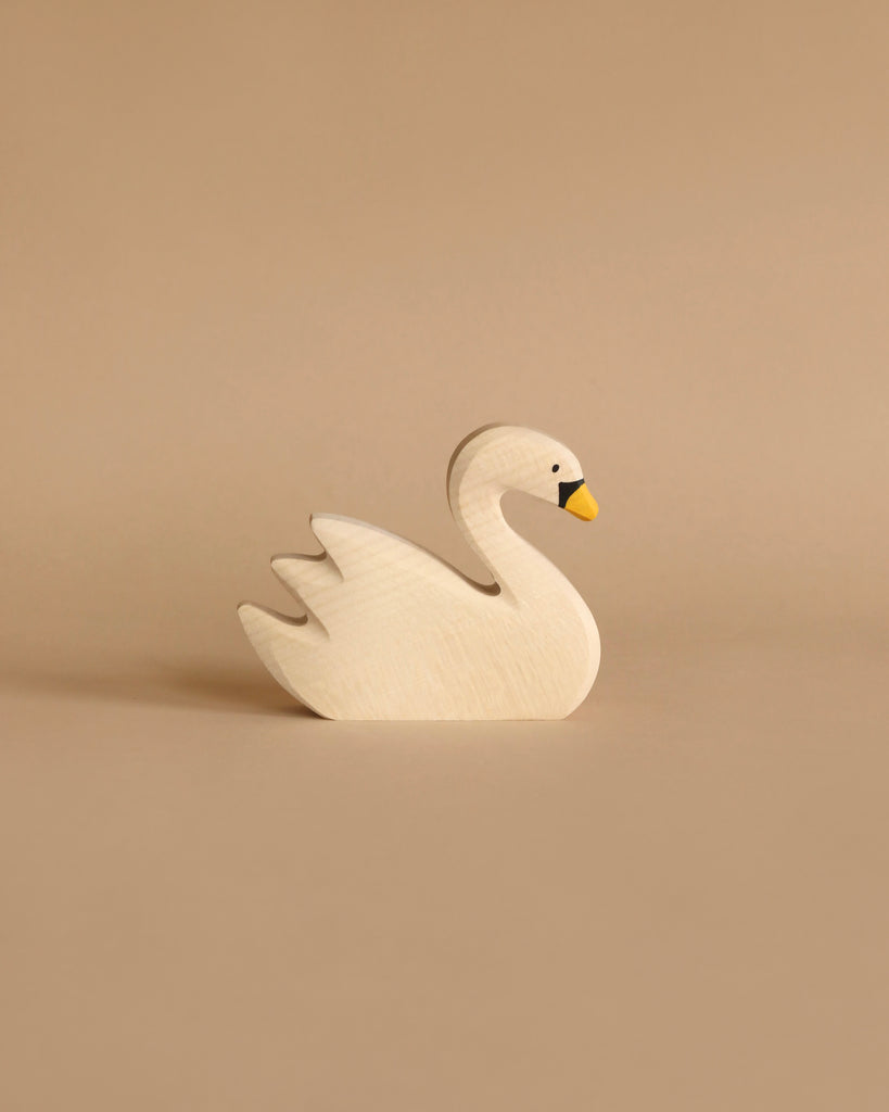 A minimalist Holztiger Swan, Swimming with a simplistic design featuring a white body, a yellow beak, and black eyes. This handcrafted wood toy is made in Europe and displayed on a beige background.