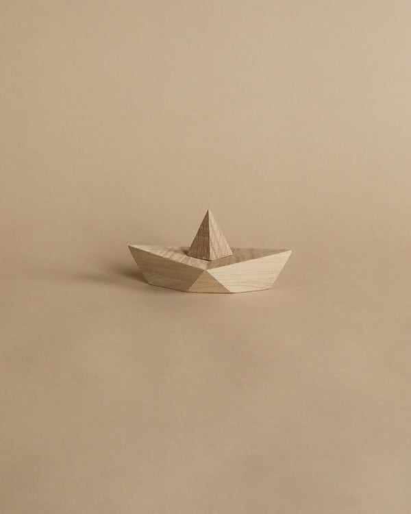 Sentence with Product Name: A Boyhood Admiral, Small Oak origami-style boat on a plain beige background, featuring a neatly folded design with geometric symmetry and visible wood grain.