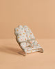 The Maileg My Babysitter - Multi Dots features a small baby sitter chair with colorful polka dots on white cotton fabric and a simple metal base, set on a beige surface with a matching beige background.