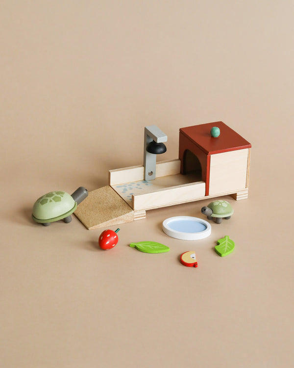 A wooden toy set arranged on a beige background, featuring a Tender Leaf dolls house, seesaw, Tortoise Pet Set, ladybug, leaves, a bird, and a water bowl.
