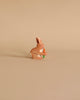 A small, brown rabbit from the Holztiger Handmade Wooden Animal Play Set holds an orange carrot on a plain beige background, highlighting European craftsmanship.