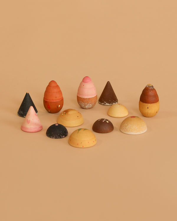 The Grapat Play Set - Bakes features assorted dome- and cone-shaped pieces in various colors and patterns, reminiscent of hand-painted wooden toys, arranged in rows on a plain beige background.