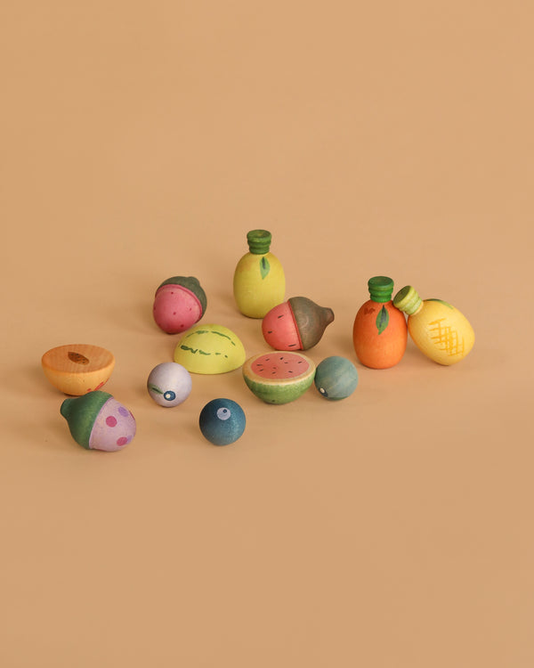 The Grapat Play Set - Fruits, featuring colorful wooden pieces like watermelon, orange, lemon, pineapple, blueberries, and acorns for open-ended play, is displayed on a plain beige background.