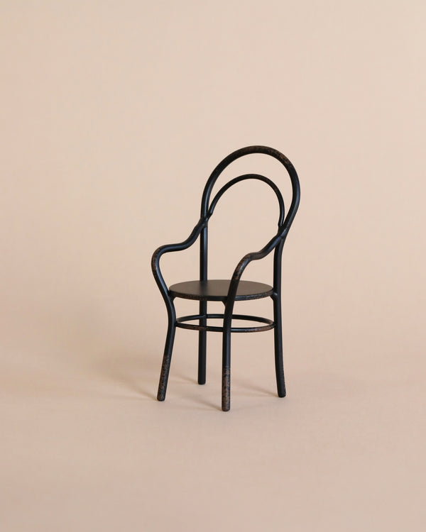 A minimalist image of a single, elegant, Maileg | Chair with Armrest set against a light beige background.