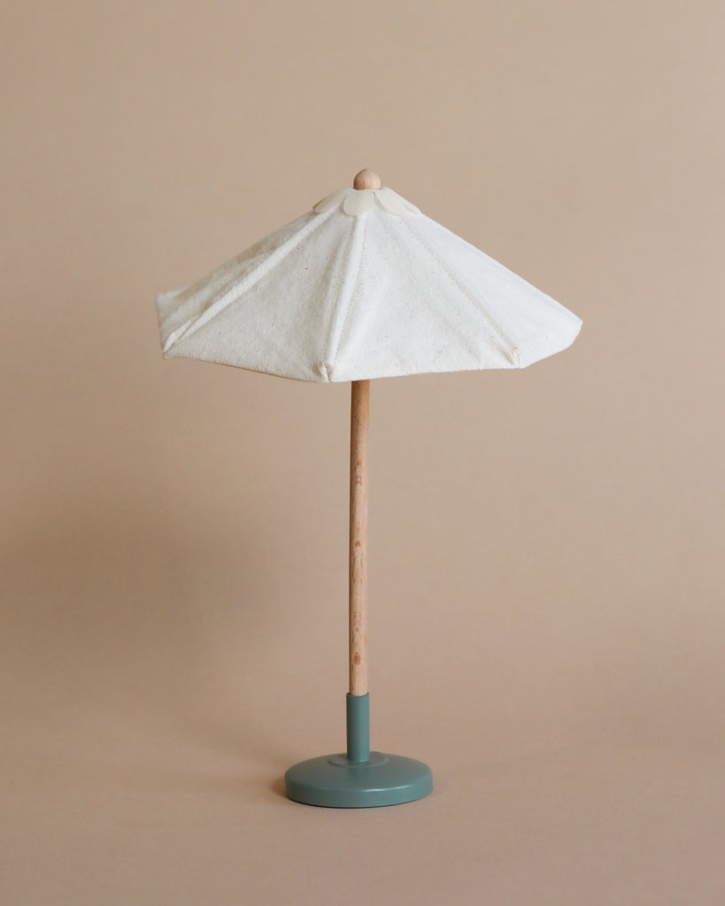 The Maileg Bonus Room Bathroom Set features a small decorative umbrella with a white canopy, wooden pole, and round teal base—ideal for Maileg House of Miniature or as charming dollhouse accessories. Set against a plain beige background.