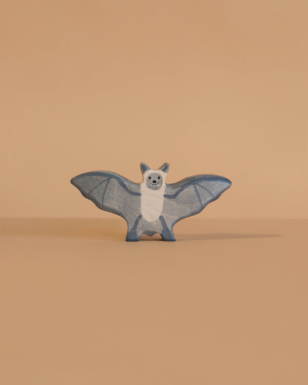 The Holztiger Bat is a small, blue and white wooden figurine with outstretched wings, standing on a smooth light beige surface against a matching background. This handcrafted toy captures the classic style of HOLZTIGER figures.