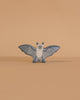 The Holztiger Bat is a small, blue and white wooden figurine with outstretched wings, standing on a smooth light beige surface against a matching background. This handcrafted toy captures the classic style of HOLZTIGER figures.