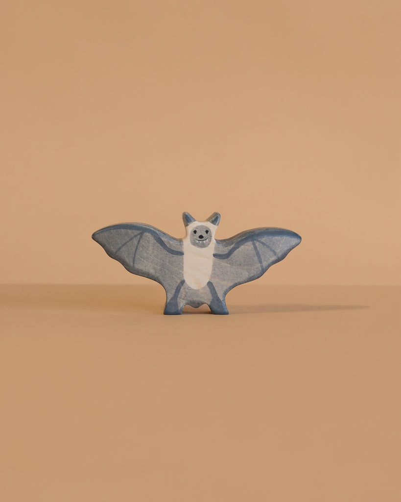 The Holztiger Bat is a small, blue and white wooden figurine with outstretched wings, standing on a smooth light beige surface against a matching background. This handcrafted toy captures the classic style of HOLZTIGER figures.
