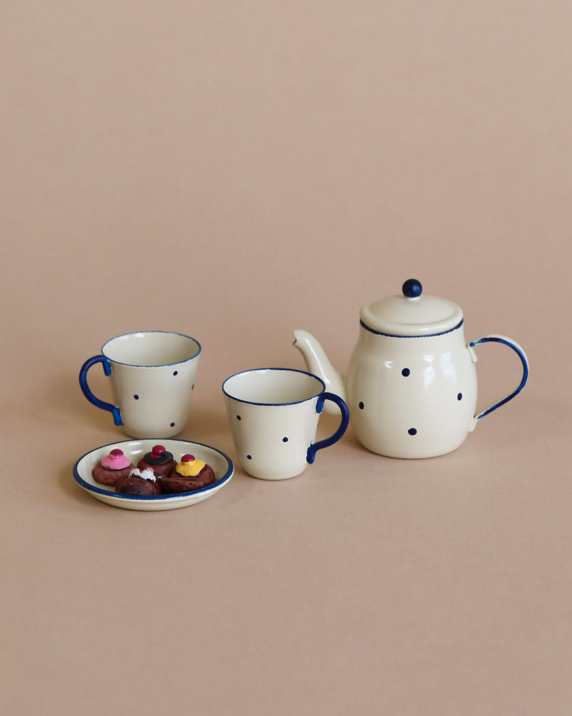 A Maileg | Miniature Tea & Biscuits for Two with a spotted design, featuring a teapot and two cups with saucers on a beige background. One saucer holds colorful candies.