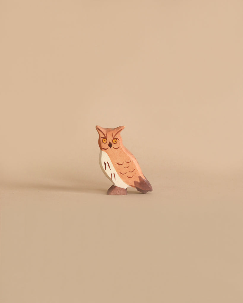 A small, brown and white owl figurine from the Holztiger Handmade Wooden Woodland Animals Set stands against a beige background, evoking the charm of classic wooden animal toys.