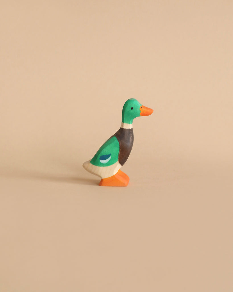 A Holztiger Mallard featuring a green head, brown neck, and orange beak stands on a plain beige background. The handcrafted wood duck has vibrant colors and is crafted in a simple, minimalist style, reminiscent of HOLZTIGER figures made in Europe.