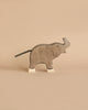 A gray, handmade wooden elephant from the Holztiger Handmade Wooden Safari Animals Set stands on a beige surface with white feet and a black tail, inspired by classic Holztiger figures and crafted from maple and beech wood.