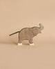 A wooden toy elephant handcrafted out of maple and beech wood stands against a beige background. The Holztiger Small Elephant, Trunk Raised, resembling HOLZTIGER figures, has a simple design with white accents on its feet and a short, black tail. Its minimalist style gives it a charming and rustic look.