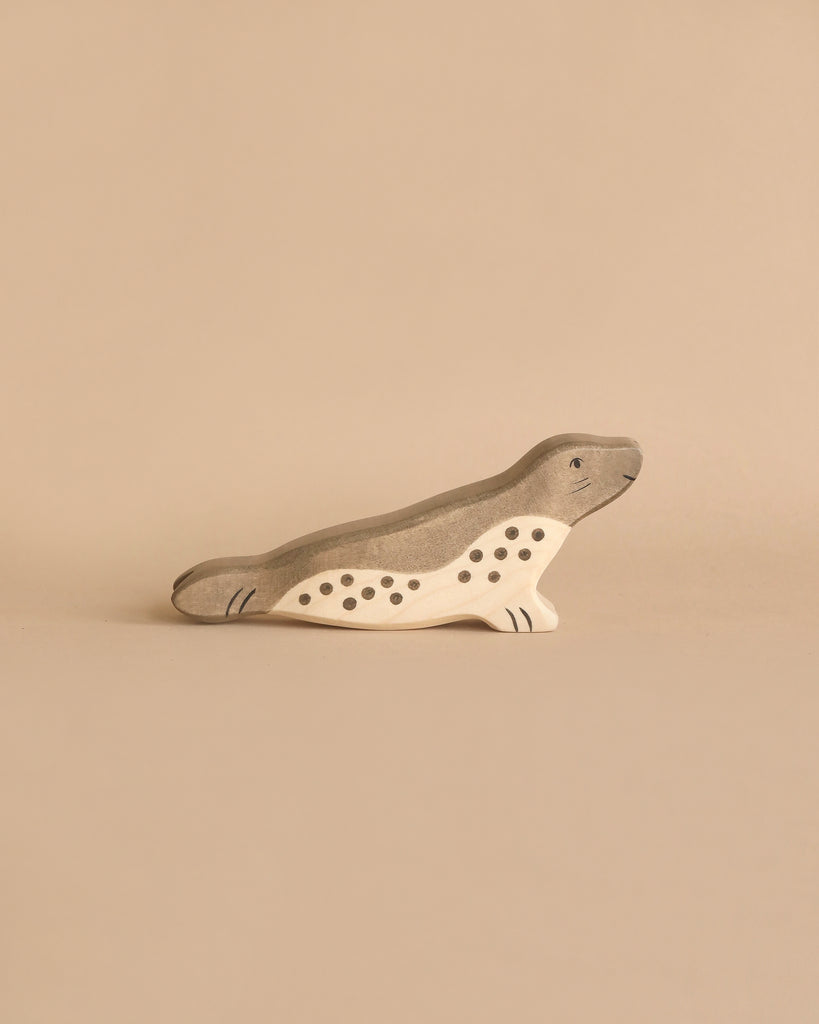 A Holztiger Handmade Wooden Ocean Animals Set toy seal with grey and natural wood coloring and painted spots.