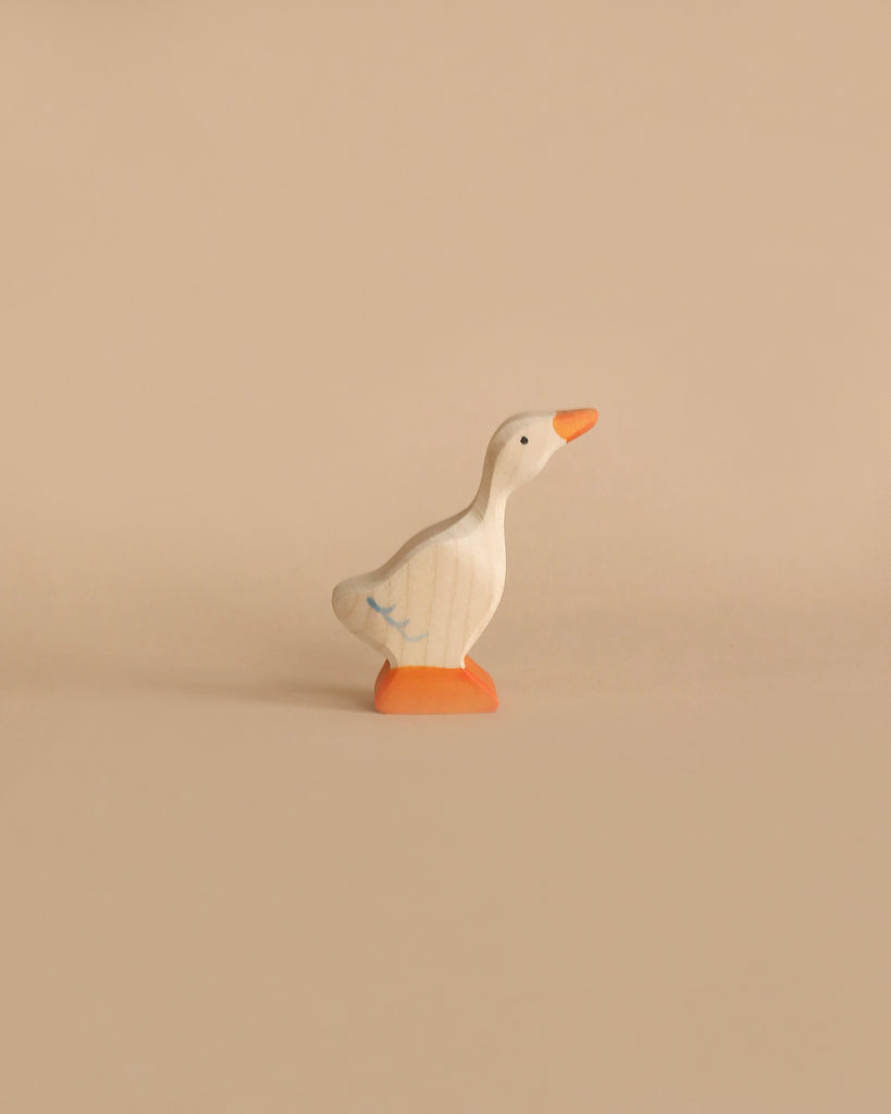 A small duck from the Holztiger Handmade Wooden Woodland Animals Set, featuring an orange beak and feet, stands on a plain beige surface—perfect for imaginative, open-ended play.